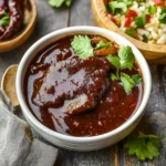 Deep red homemade adobo sauce in glass jar with wooden spoon